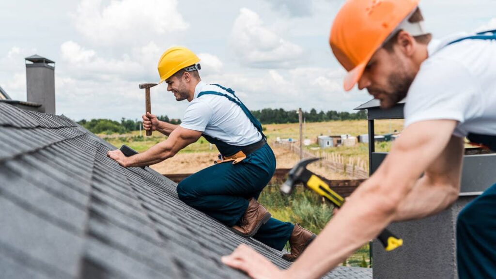 Roof crew members nailing asphalt shingles down