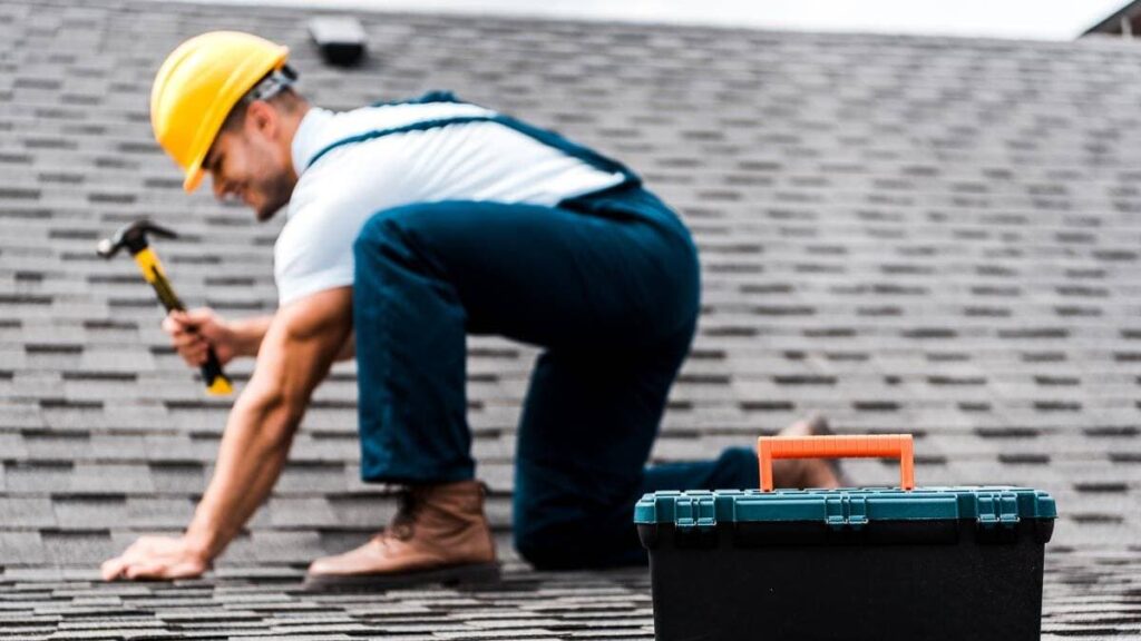 A roofing crew member nailing down shingles